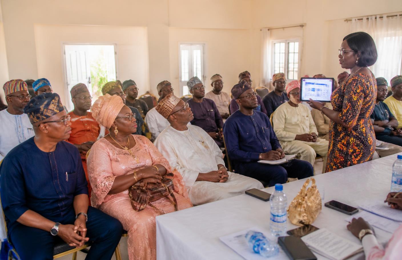 A town union meeting where the financial secretary presents figures from a tablet